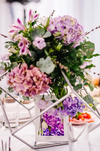 Table de fête décorée d'une composition de fleurs violettes, violettes, roses et de verdure dans la salle de banquet. Table les jeunes mariés de la région lors d'une fête de mariage.