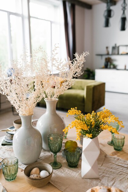 Table de fête de Pâques fleurs de mimosa dans un vase et des œufs de nourriture traditionnelle à l'intérieur du salon lumineux