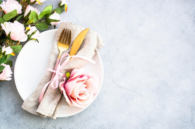 Table de fête servant avec des couverts modernes en assiette blanche et des fleurs roses vue de dessus en blanc avec espace de copie
