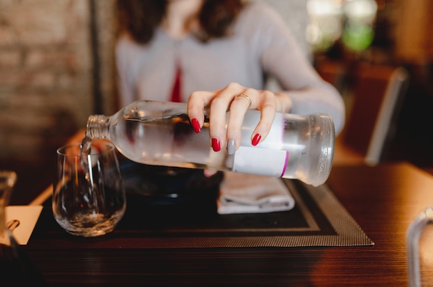 table de gros plan dans le restaurant. Main de femme méconnaissable tenant une bouteille versant de l'eau fraîche dans le verre.