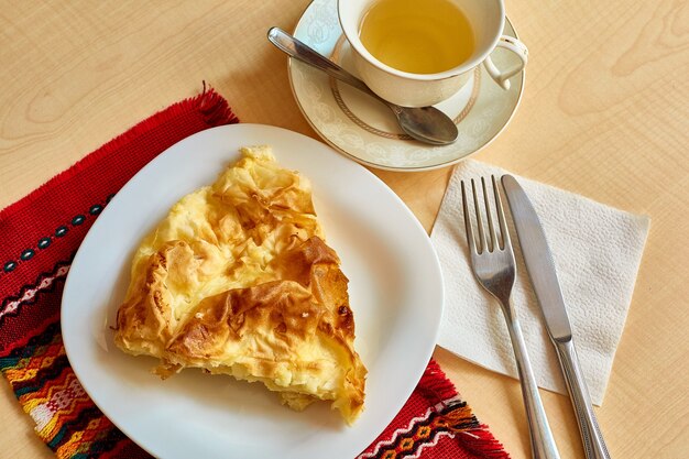 Sur la table il y a une omelette dans une assiette, une tasse de thé avec une soucoupe et une cuillère à café, un couteau et une fourchette sur une serviette