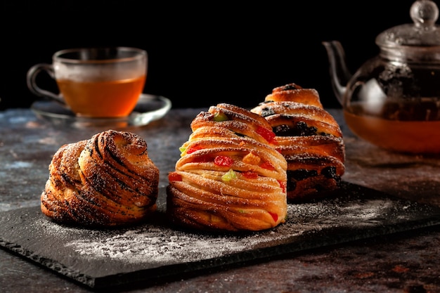 Sur la table, des kraffins aux raisins secs, fruits confits et graines de pavot, saupoudrés de sucre en poudre.