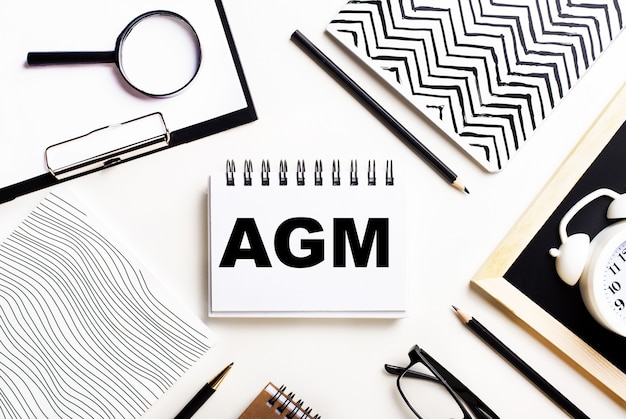 Sur une table lumineuse se trouvent des cahiers, une loupe, un réveil, des lunettes et un stylo. Et au centre se trouve un cahier avec le texte AGM