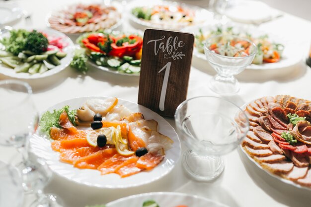 Table de mariage décorée et numérotée avec de la nourriture, des boissons, des appareils électroménagers et des fleurs.