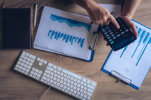 La table moderne de bureau de travail de bureau, les mains d&#39;affaires emploie la calculatrice pour vérifier le diagramme un