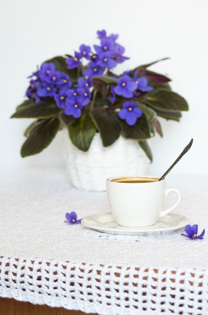 Photo table avec une nappe blanche avec une fleur de violette africaine et une tasse de café noir.