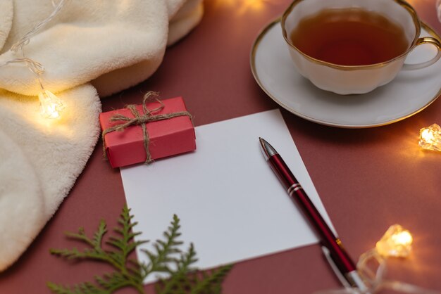 Table de Noël avec carnet, feuille de papier vierge, tasse de thé et boîte-cadeau.