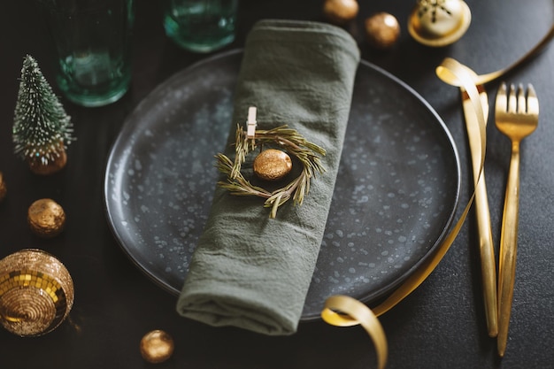 Table de Noël servie dans des tons sombres avec une déco dorée.