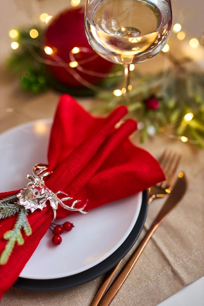 Table de Noël traditionnelle mise en place de près. Couverts dorés, serviette en lin avec anneau de cerf, branches d'épicéa et verre de vin. Fond de vacances. Mise au point sélective, guirlande, bokeh.