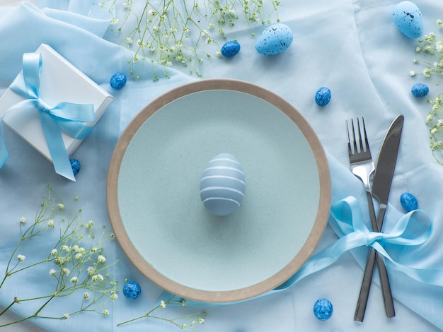Table de Pâques festive avec des œufs, des fleurs et une boîte à cadeaux sur fond bleu