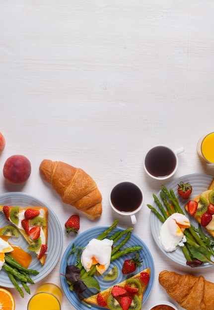 Table avec petit-déjeuner - asperges aux œufs pochés, pain grillé aux fruits, croissants, café, jus