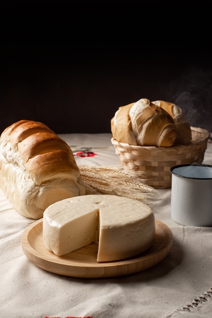 Table de petit-déjeuner au Brésil avec pains, fromage, tasse de café et accessoires sur une nappe légère avec broderie.