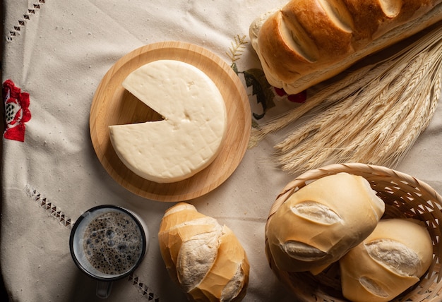 Table de petit-déjeuner au Brésil avec pains, fromage, tasse de café et accessoires sur une nappe légère avec broderie.