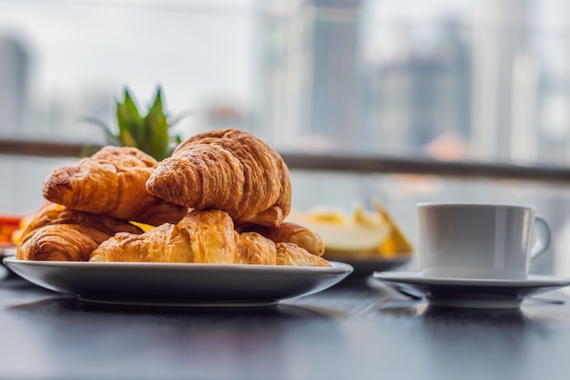 Table de petit-déjeuner avec café, fruits et pain croissant sur un balcon dans le contexte de la grande ville