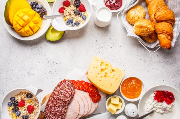 Table de petit-déjeuner continental avec croissants, confiture, jambon, fromage, beurre, granola et fruits, espace de copie.