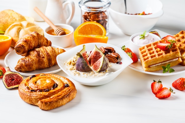 Table de petit déjeuner avec des flocons d'avoine, des gaufres, des croissants et des fruits.