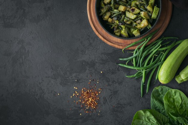 Table de petit-déjeuner sain avec des légumes frits dans une poêle et ingrédient pour la cuisson sur une surface sombre vue de dessus copie espace