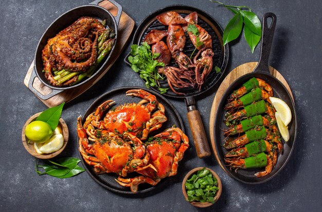 Photo table avec des plats de fruits de mer, des crabes cuits, des crevettes tigres, des pieuvres grillées et des calamars sur une casserole en fonte.