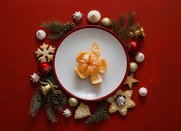 Table de réglage de Noël et du nouvel an. Assiette vide blanche avec couverts et branches d'arbres de Noël, serviette rouge sur fond de béton rouge.