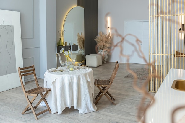 Une table romantique est servie pour deux dans la cuisine dans un appartement ouvert lumineux de style moderne avec des murs légers et des planchers en bois