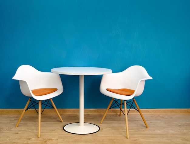 Table ronde intérieure moderne et deux chaises blanches près du mur bleu.