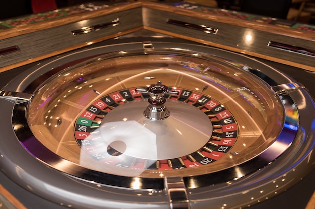 Table de roulette au casino, avec de nombreux jeux et machines à sous, roulette au premier plan. Lumière dorée et luxueuse, intérieur de casino. Le jeu consiste à parier de l'argent ou à jouer à des jeux de hasard pour de l'argent