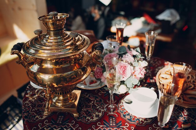 Table russe traditionnelle pour boire du thé avec un samovar, des verres de vin, des fleurs, des pâtisseries, des bagels et des petits pains