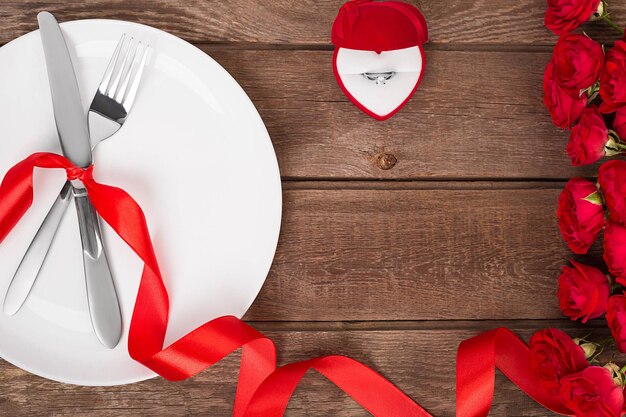 Table de Saint Valentin avec assiette, fourchette, couteau, bague, ruban et roses. Fond de Saint Valentin. Nature morte