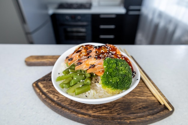 Sur la table se trouve une assiette de riz trois crevettes royales haricots verts et brocoli sur une planche à découper en bois en forme de hache Le tout garni de sauce unagi Concept de cuisine asiatique