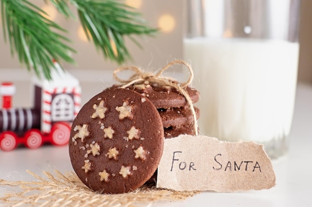 Sur la table se trouve une pile de biscuits de Noël au chocolat ronds et un verre de lait