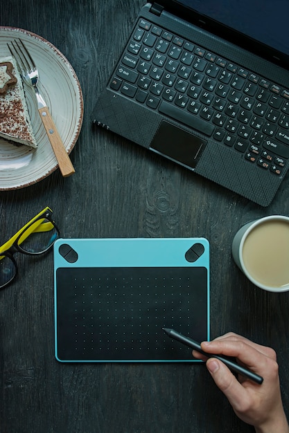 Sur la table se trouvent un ordinateur portable, une tablette graphique et une tasse de café.