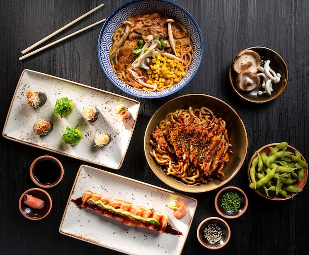 Table avec sushis typiques de la cuisine japonaise, tataki de saumon, soupe miso, nouilles croustillantes au poulet, edamame. Vue d'en haut.