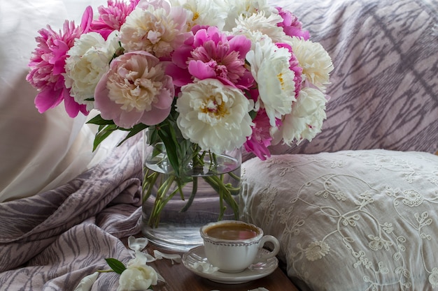 sur la table, une tasse de café et un bouquet de pivoines