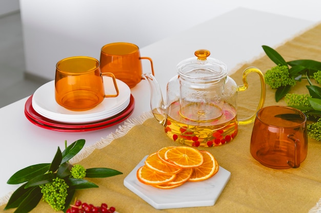 Une table avec des tasses en verre orange une théière avec des fruits et des baies de thé