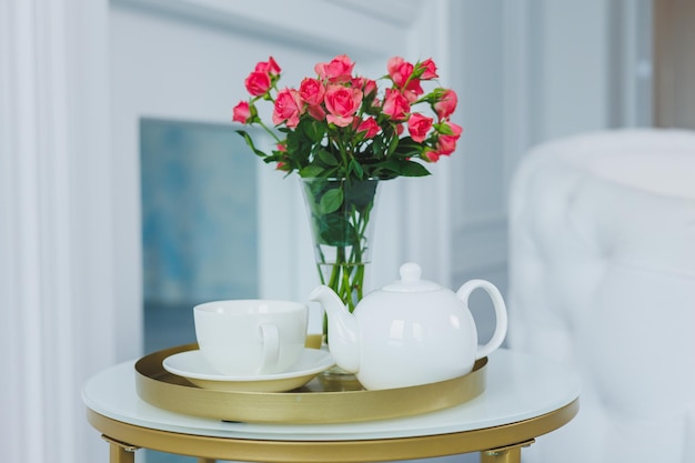 Une table avec une théière blanche et une tasse blanche sur la table un vase avec des fleurs fraîches