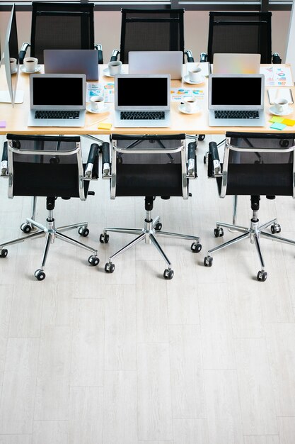 Table de travail de la salle de réunion de conférence dans le bureau de l'entreprise rempli d'ordinateurs portables, de tasses à café chaudes noires et de documents de documentation de données et de chaises noires avec espace de copie sur plancher en bois.