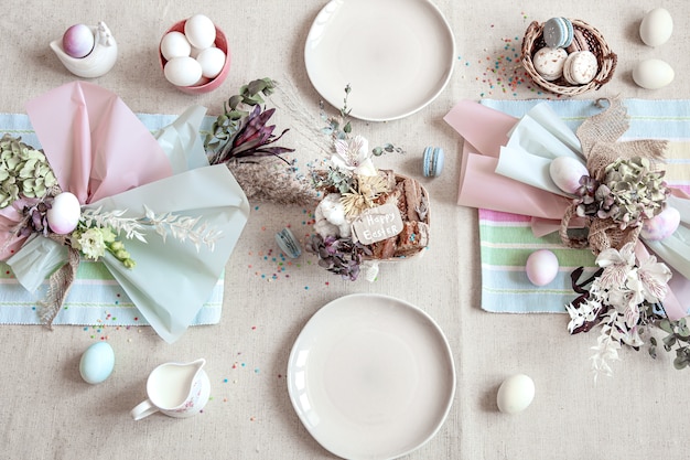 Table de vacances décorée avec assiettes blanches, œufs et arrangement floral. Concept de joyeuses Pâques.