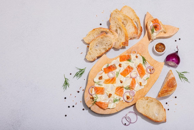 Tableau au beurre à la mode avec saumon, oignon rouge, moutarde et dill frais, collation maison avec pain baguette, concept végétarien sain pour une fête d'amis, fond en béton de pierre claire, vue supérieure