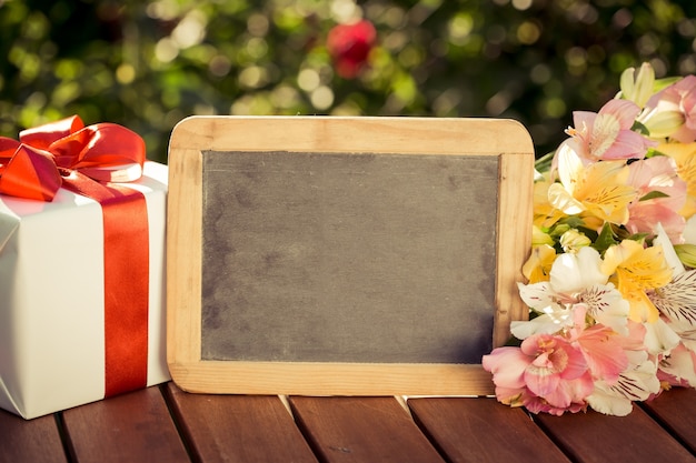 Tableau blanc, coffret cadeau et fleurs sur fond de printemps. Concept de journée de la femme.