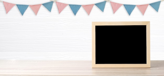 Tableau blanc debout sur les drapeaux de la fête colorée suspendus sur un fond de bois blanc avec espace de copie pour le texte