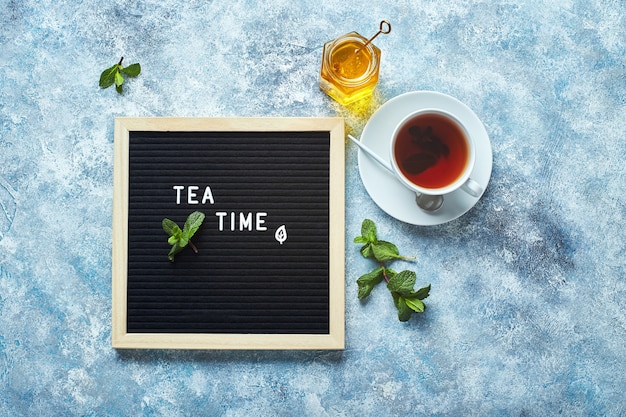 Tableau de lettres noir de l'heure du thé avec texte sur table bleue avec tasse de thé en verre aux feuilles de menthe