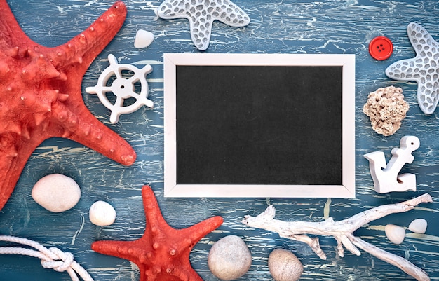 Photo tableau noir avec cadre composé de coquillages, de pierres, de corde et d'étoile de mer sur texture bleue, espace de copie