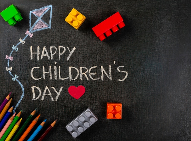 Tableau noir écrit «Happy Children's Day» et dessin de cerf-volant avec pièces d'assemblage dispersées et crayons de couleur