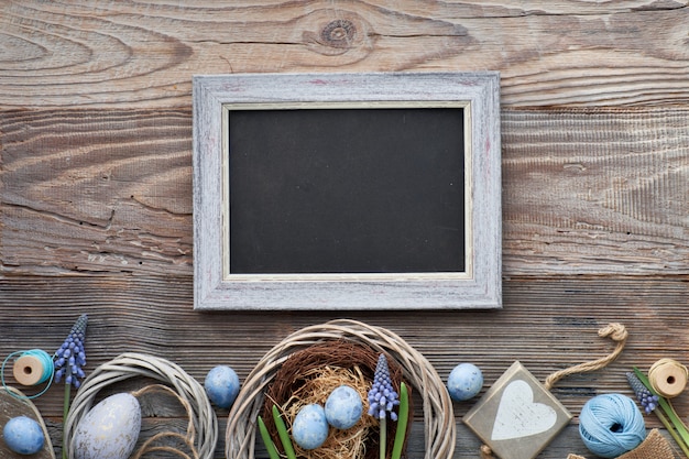 Tableau noir de Pâques avec des oeufs de Pâques, des fleurs et des décorations de printemps sur bois, espace de texte