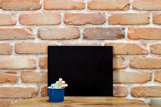 Tableau propre blanc une craie sur une table en bois au mur de briques.