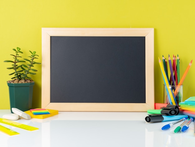 Tableau, succulent et fournitures scolaires par le mur jaune. Vue latérale, vide pour le texte.