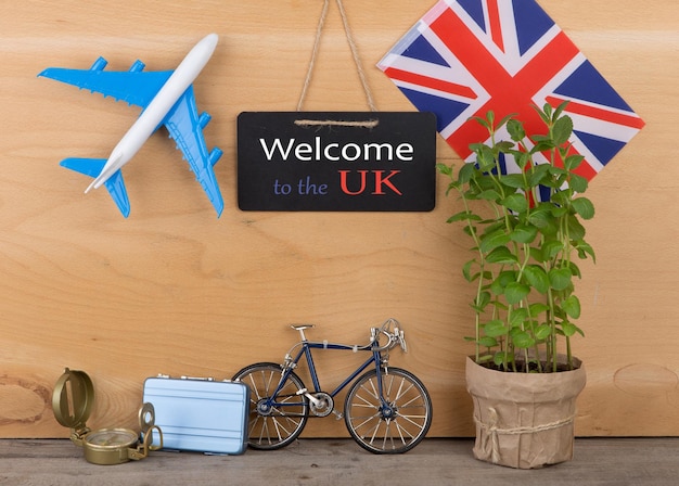 Tableau de temps de voyage avec texte Bienvenue au Royaume-Uni drapeau du Royaume-Uni modèle d'avion petit vélo et valise boussole sur fond de bois