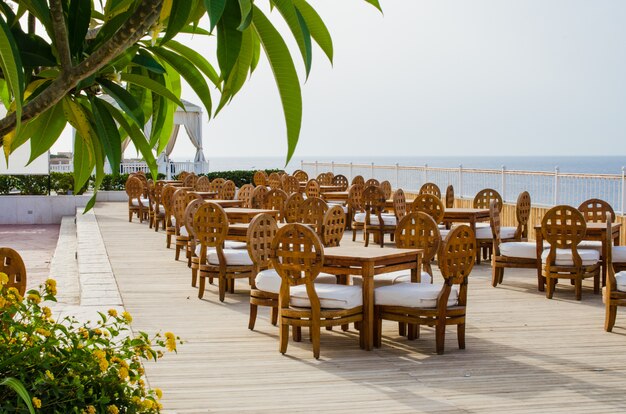 Tables et chaises en bois sur la terrasse du café d'été confortable avec vue sur la mer.