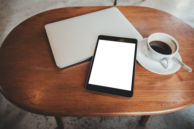 Tablet PC noir avec écran blanc de bureau blanc avec ordinateur portable et tasse de café sur la table en bois