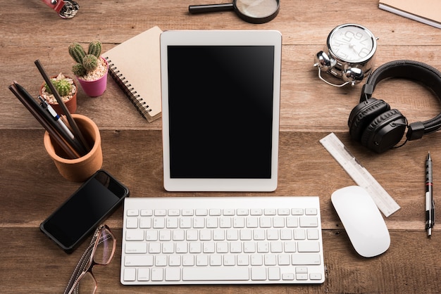 Tablette blanche avec écran blanc sur le bureau en bois avec des objets de papeterie